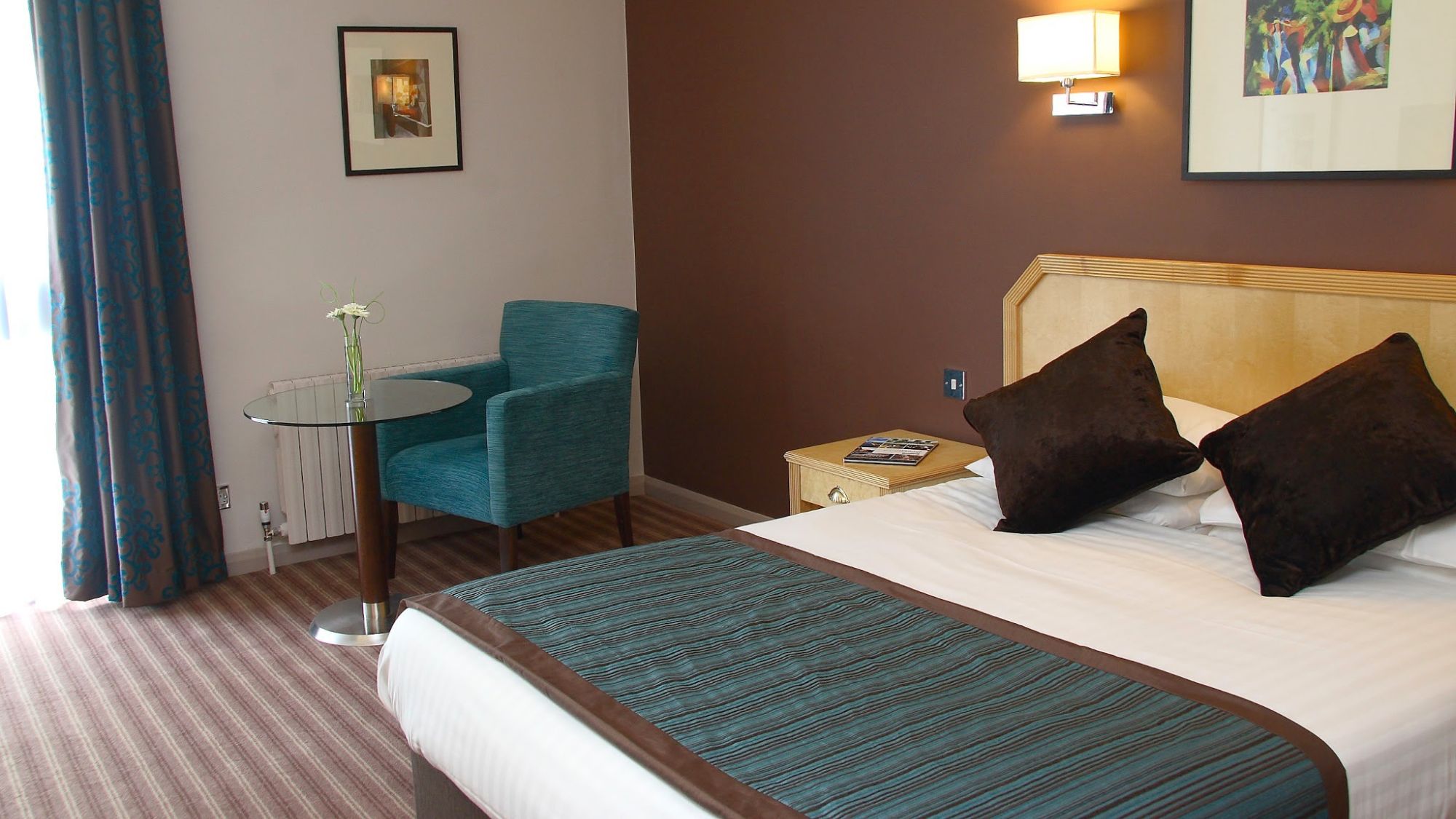 A hotel bedroom featuring a teal accent chair and a bed with a teal and grey runner.