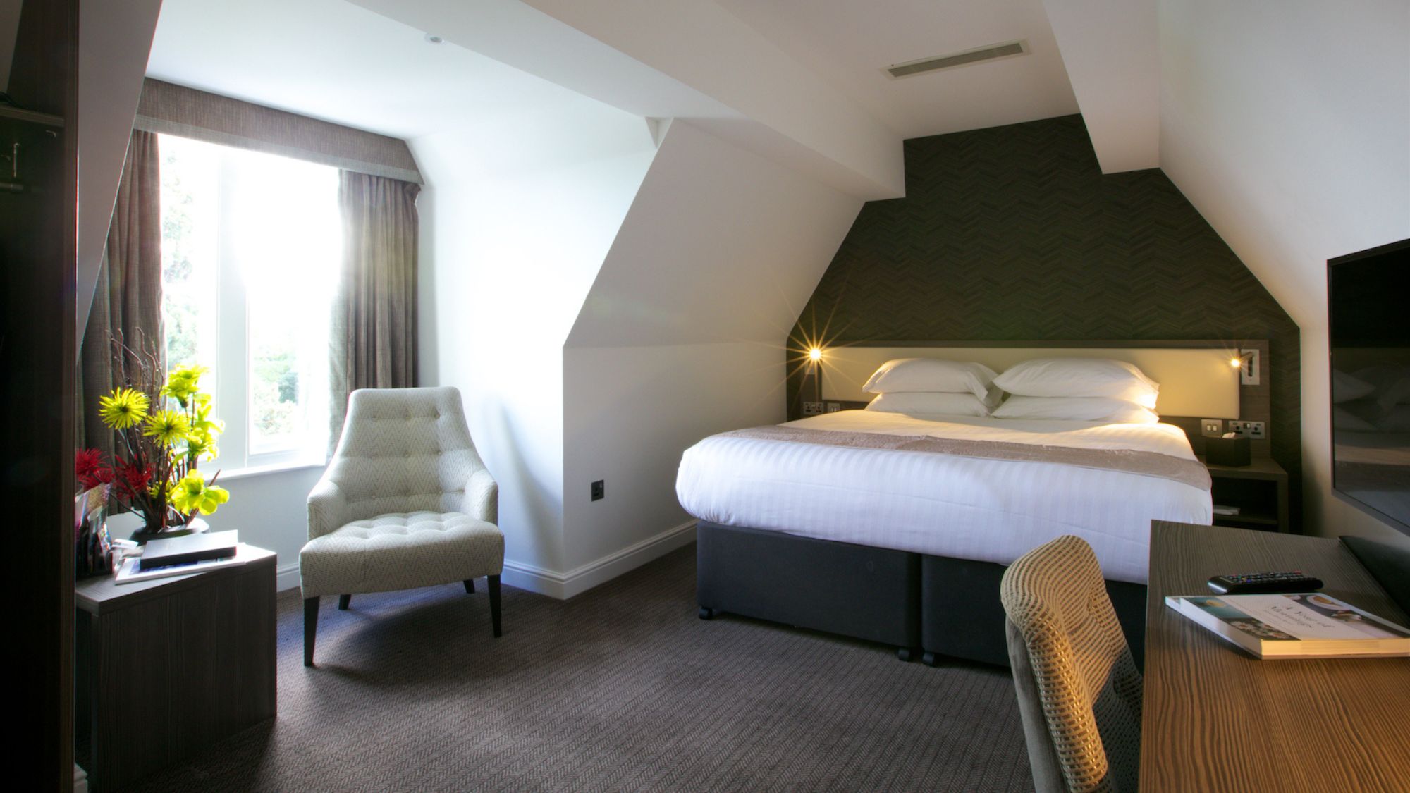 A minimalist attic-style bedroom with a white bed and a green accent wall.