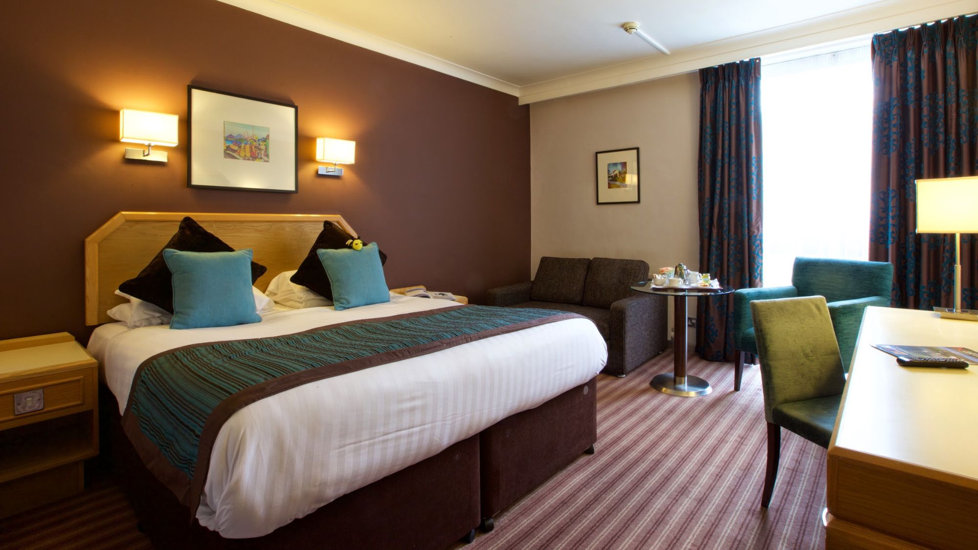A comfortable hotel room with a king-sized bed and a dark wood headboard.