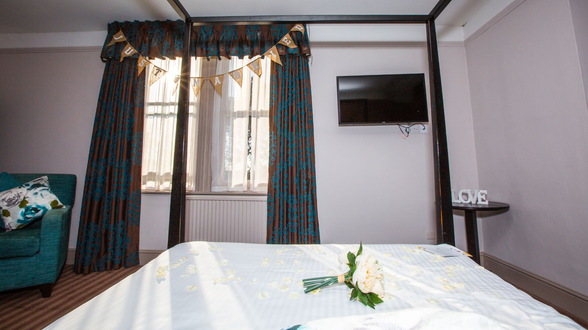 A close-up of a four-poster bed with white linens and decorative flowers.