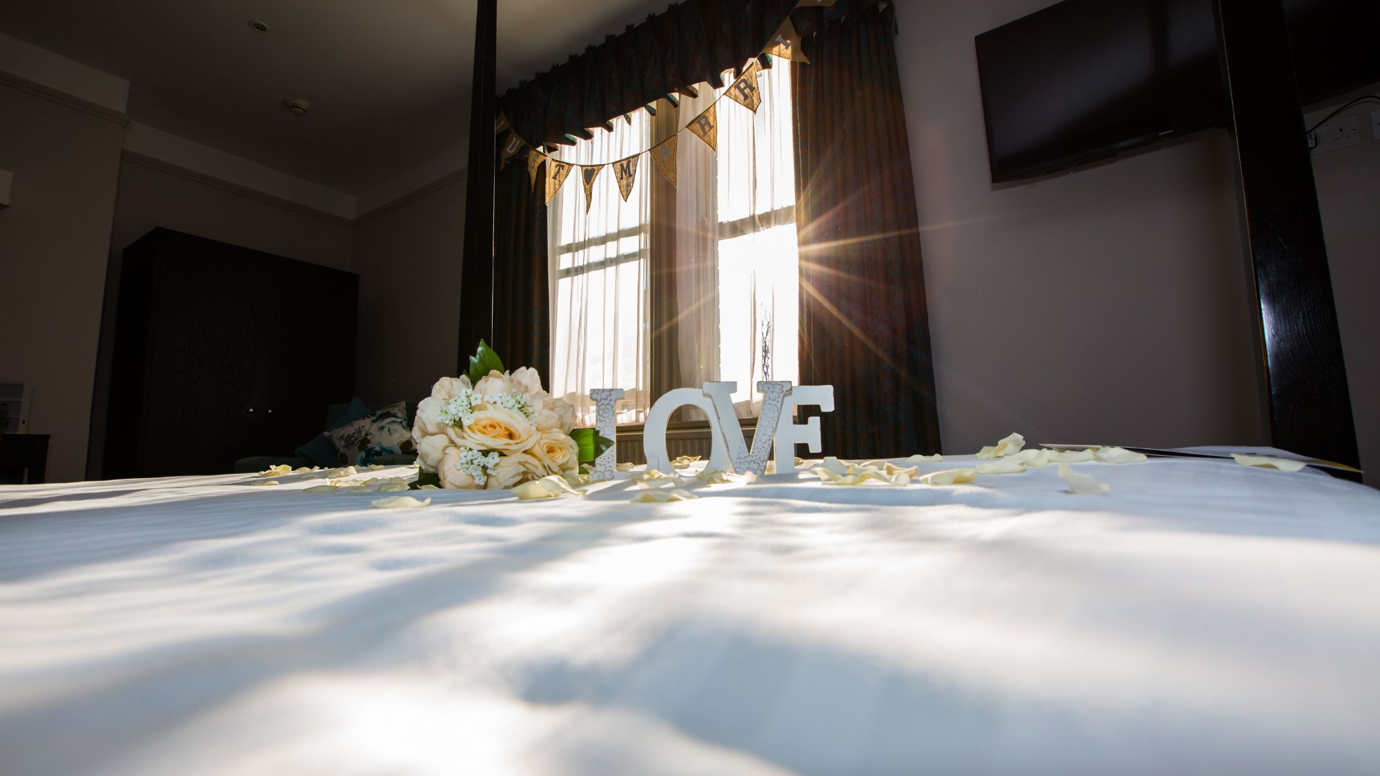 A bright hotel room with a white bed and light coming through a window.