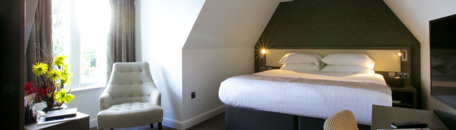 A bright bedroom with a white bed and a view of a seating area.