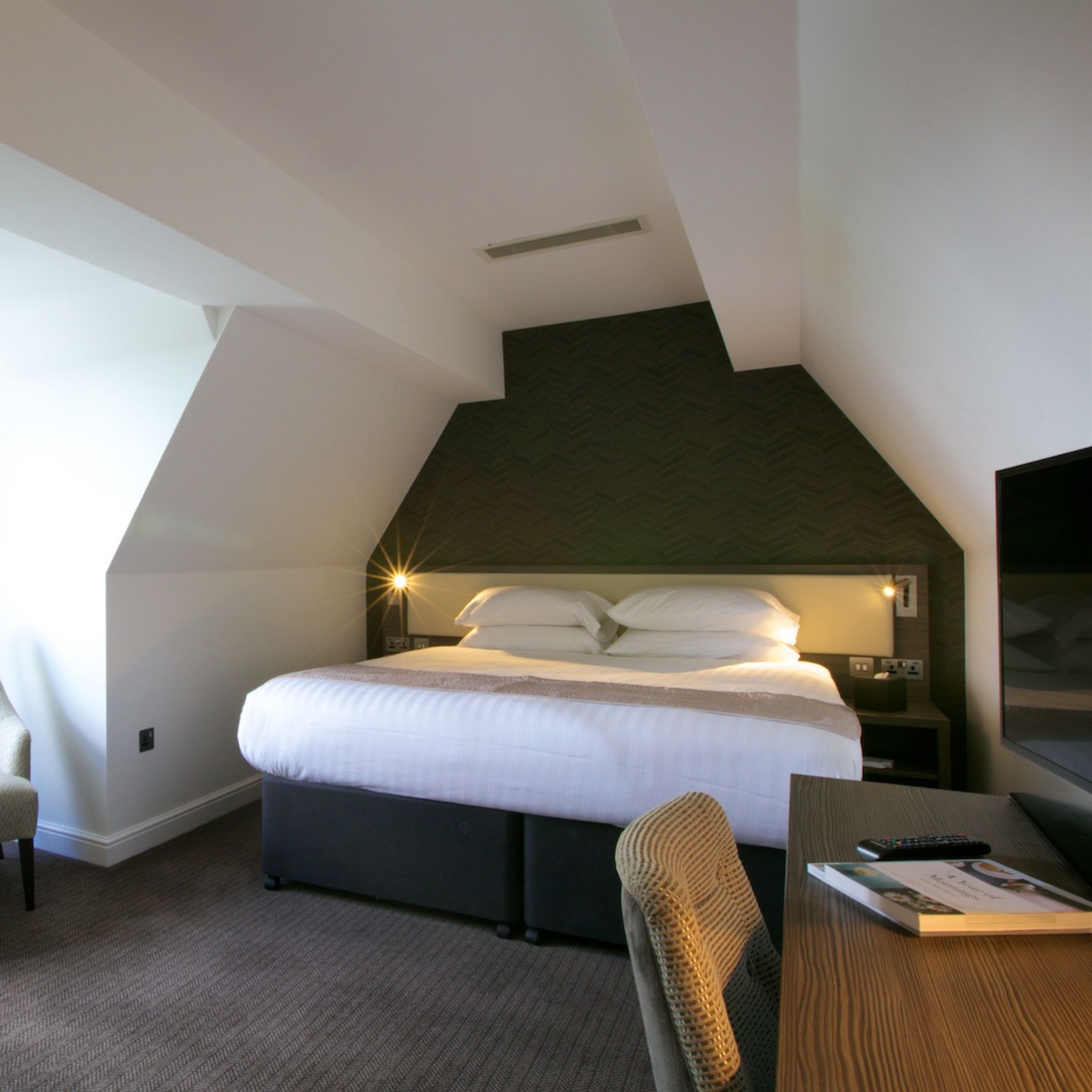 An attic-style bedroom with sloped ceilings and a large window.