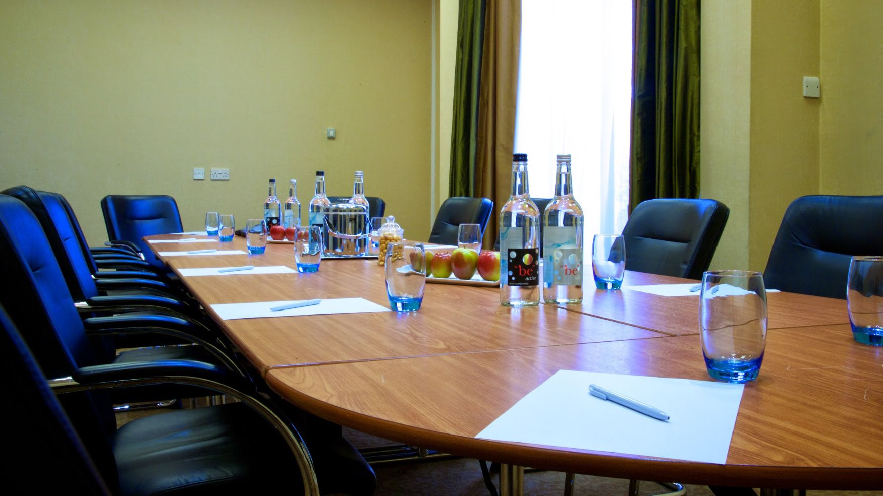 A professional meeting room with a wooden table, bottled water, and pens ready for attendees.