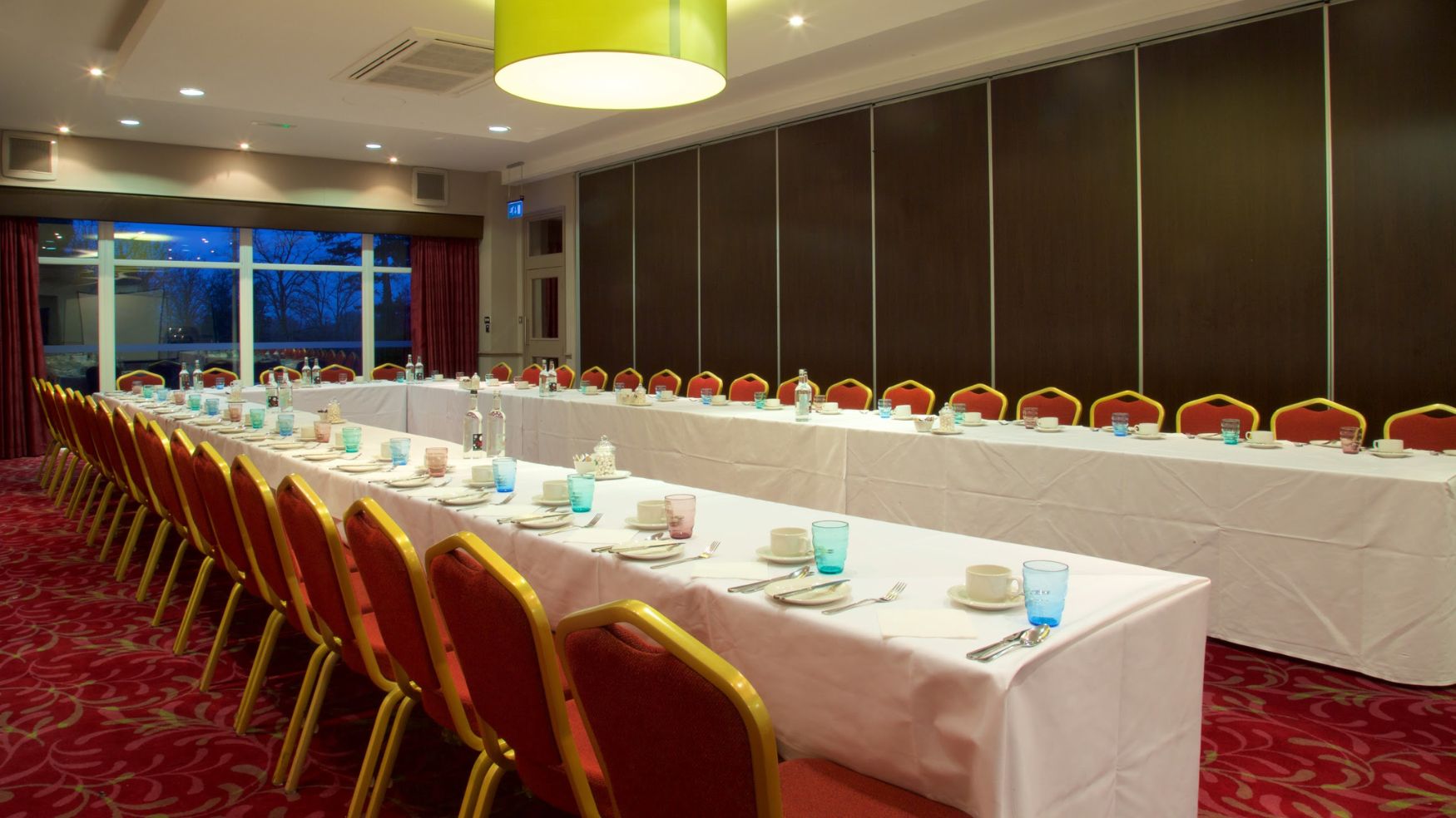 A close-up of a U-shaped conference table with white linens and red chairs.