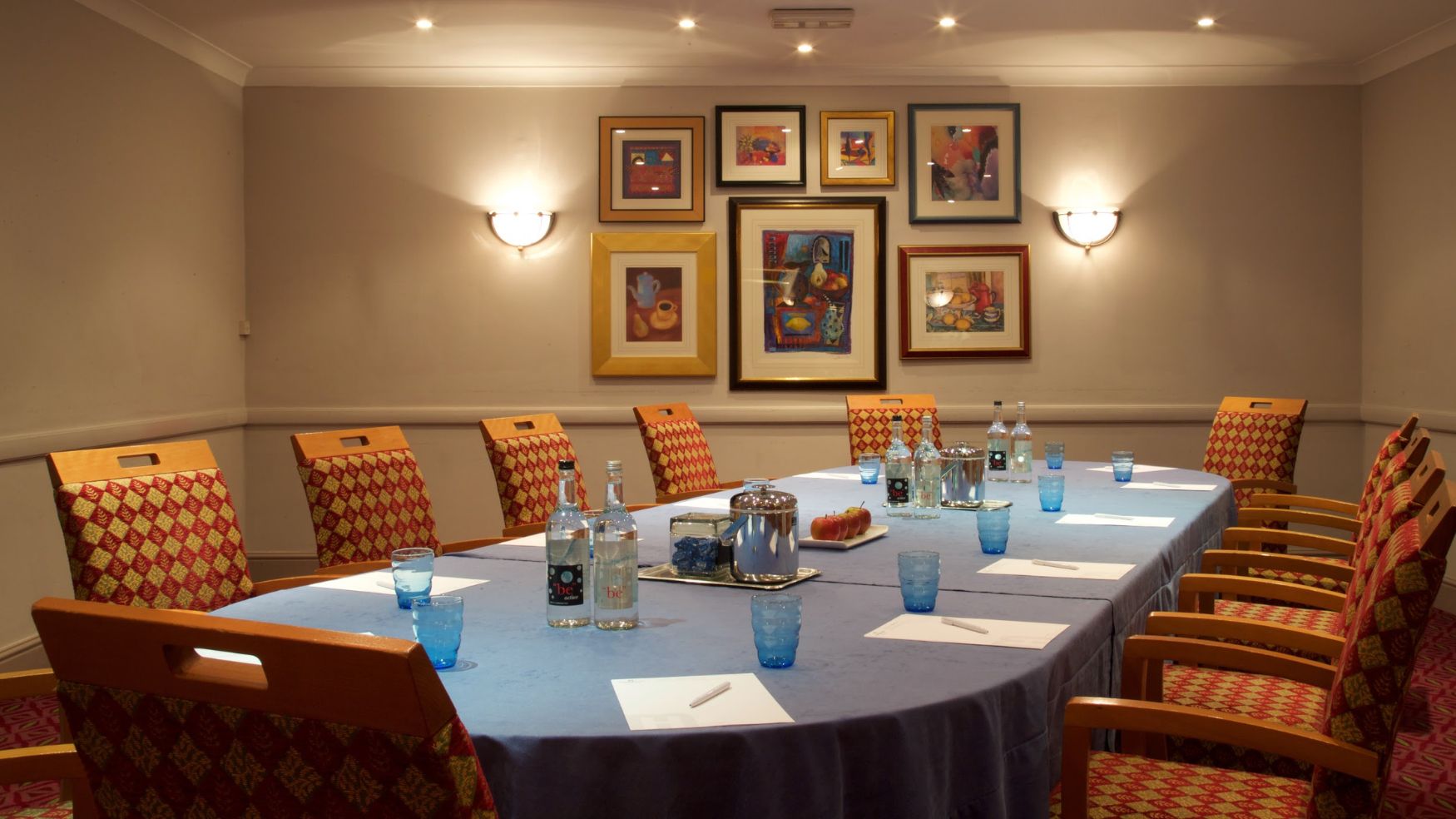 A formal boardroom setup with a long table, blue linens, and framed pictures on the wall.