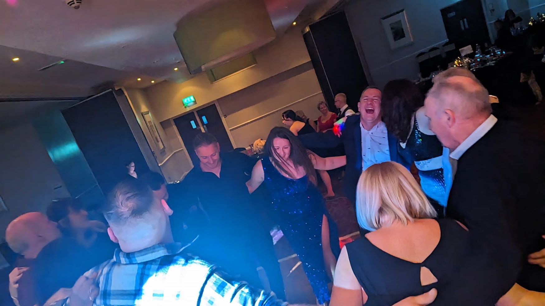People dancing and celebrating at an event with blue disco lighting.