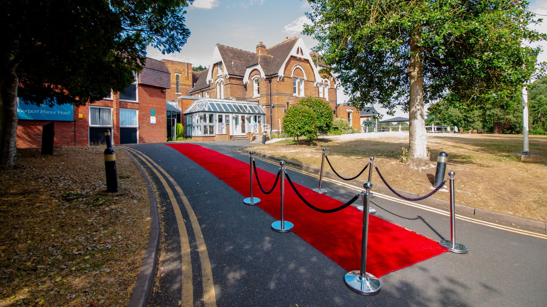 An exterior view of the manor with a red carpet and stanchions leading to the entrance.