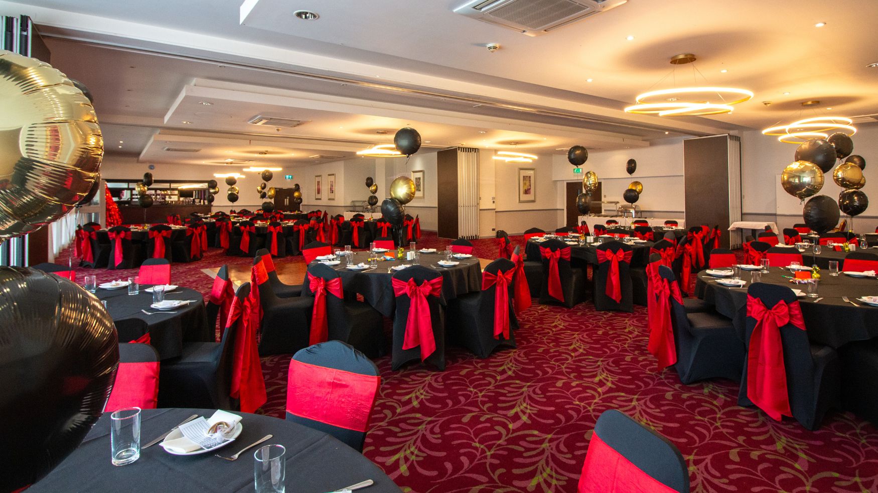 A banquet setup with black tablecloths and red accents under warm lighting.