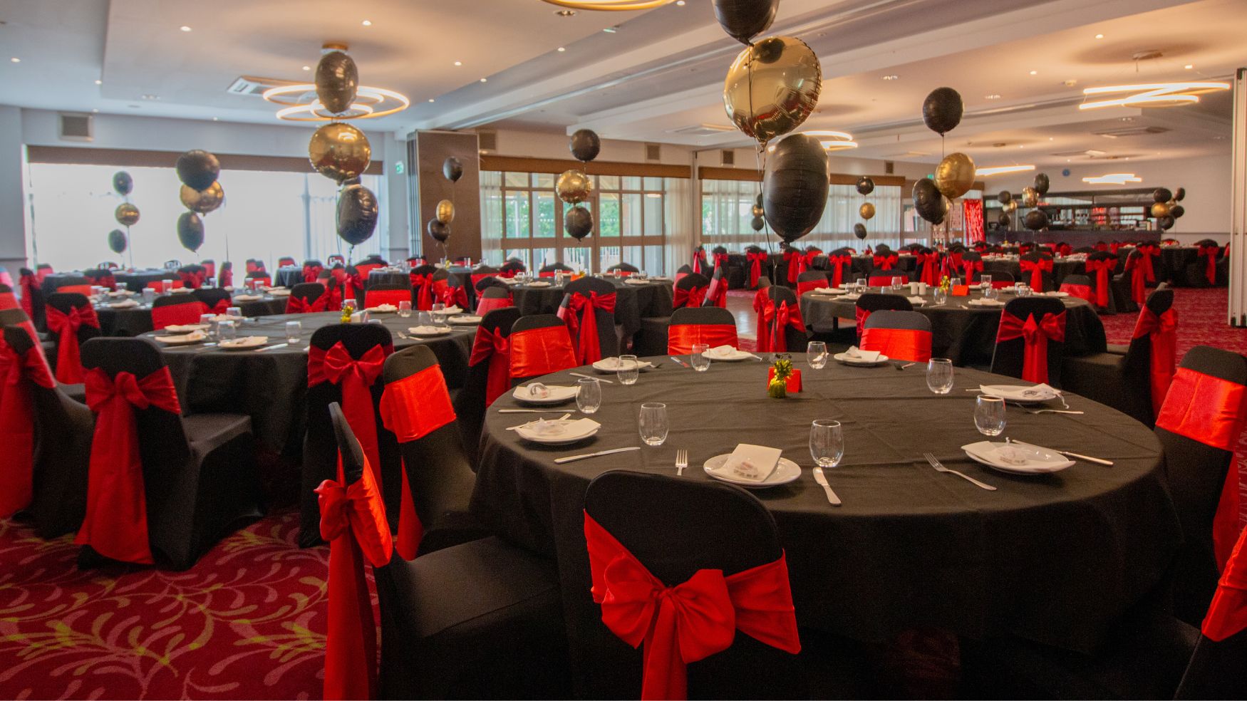 A formal dining room featuring round tables with black cloths and striking red sashes.