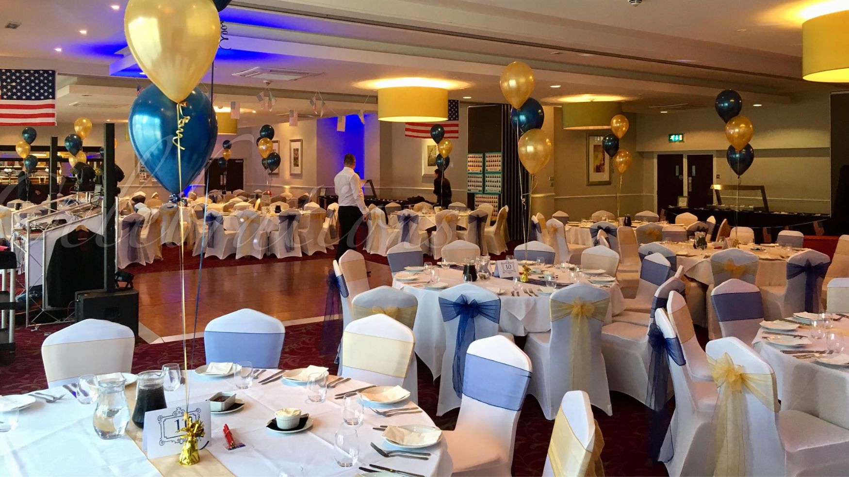 A ballroom set for a gala with white table linens and blue chair accents.