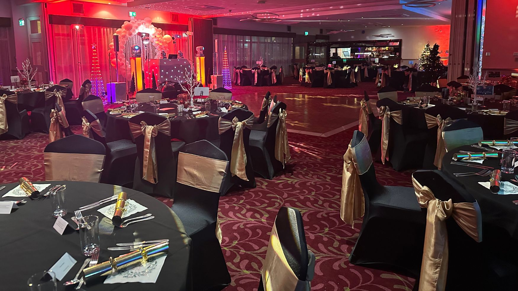 A decorated event room with round tables, black linens, and gold chair bows.