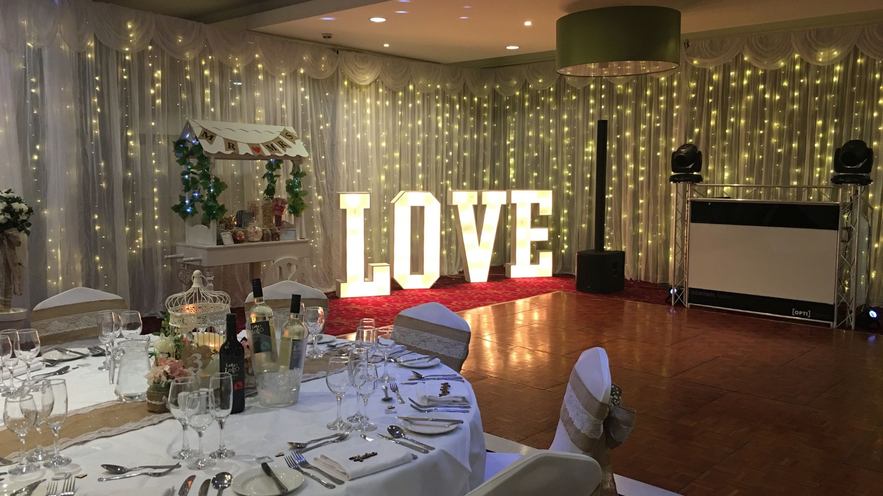 An indoor wedding scene featuring a "LOVE" marquee sign and a backdrop of fairy lights.