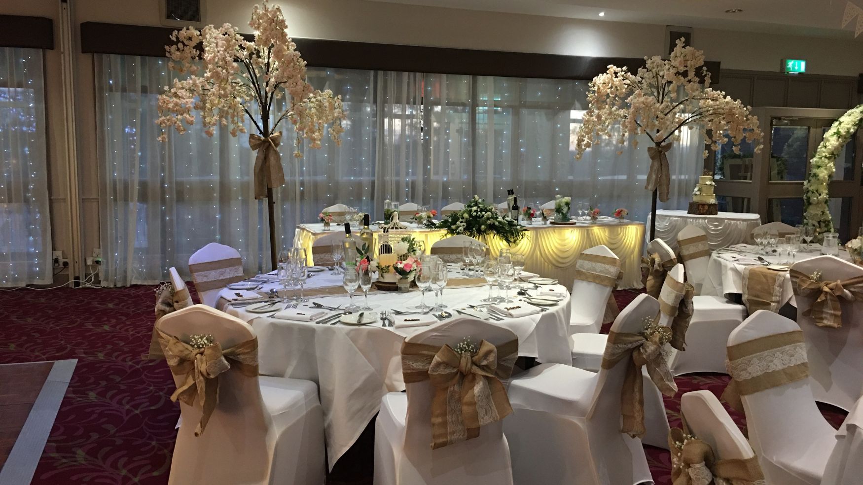 A reception table decorated with a tall floral tree centerpiece and gold accents.