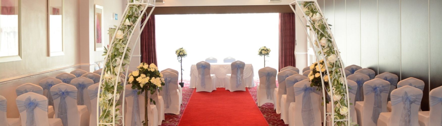 A wedding ceremony aisle with a red carpet leading to a floral arch.