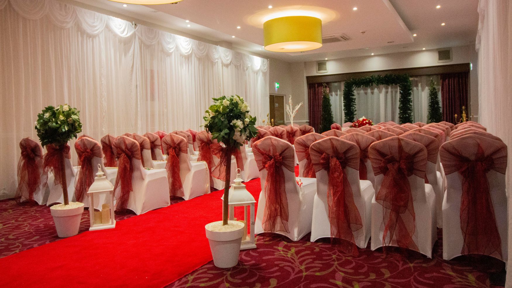 A ceremony room with a red carpet aisle and chairs adorned with red sashes.