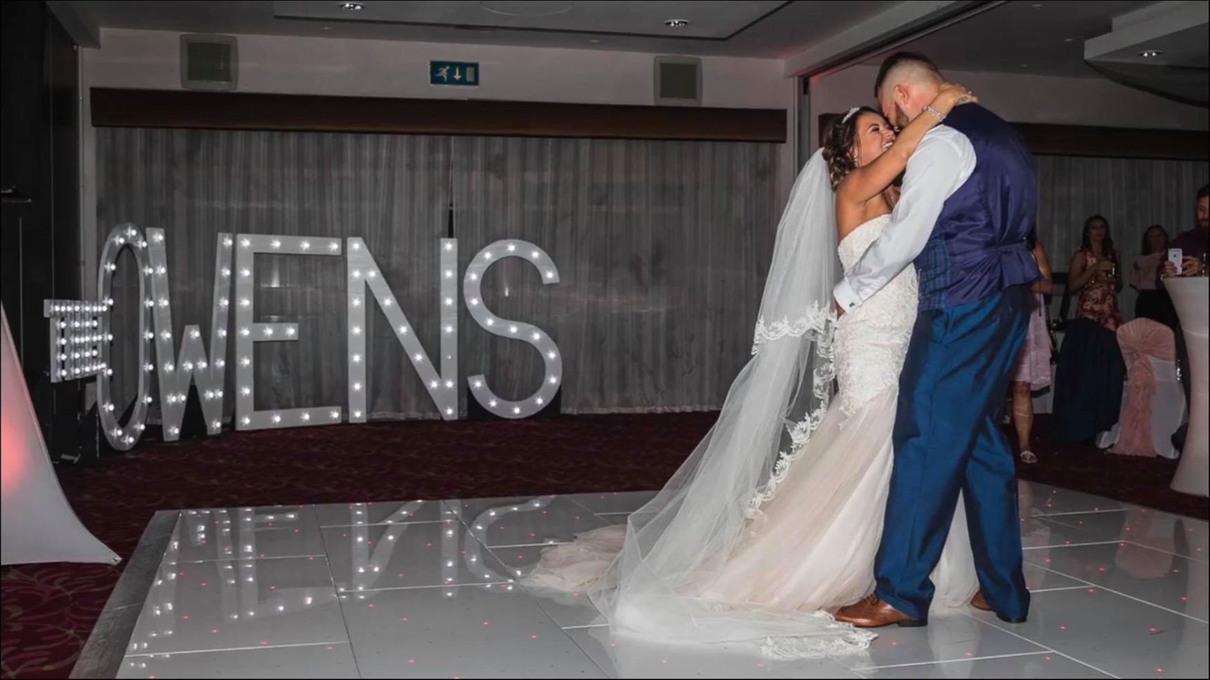 A bride and groom posing in front of large marquee letters that appear to spell "MR & MRS."