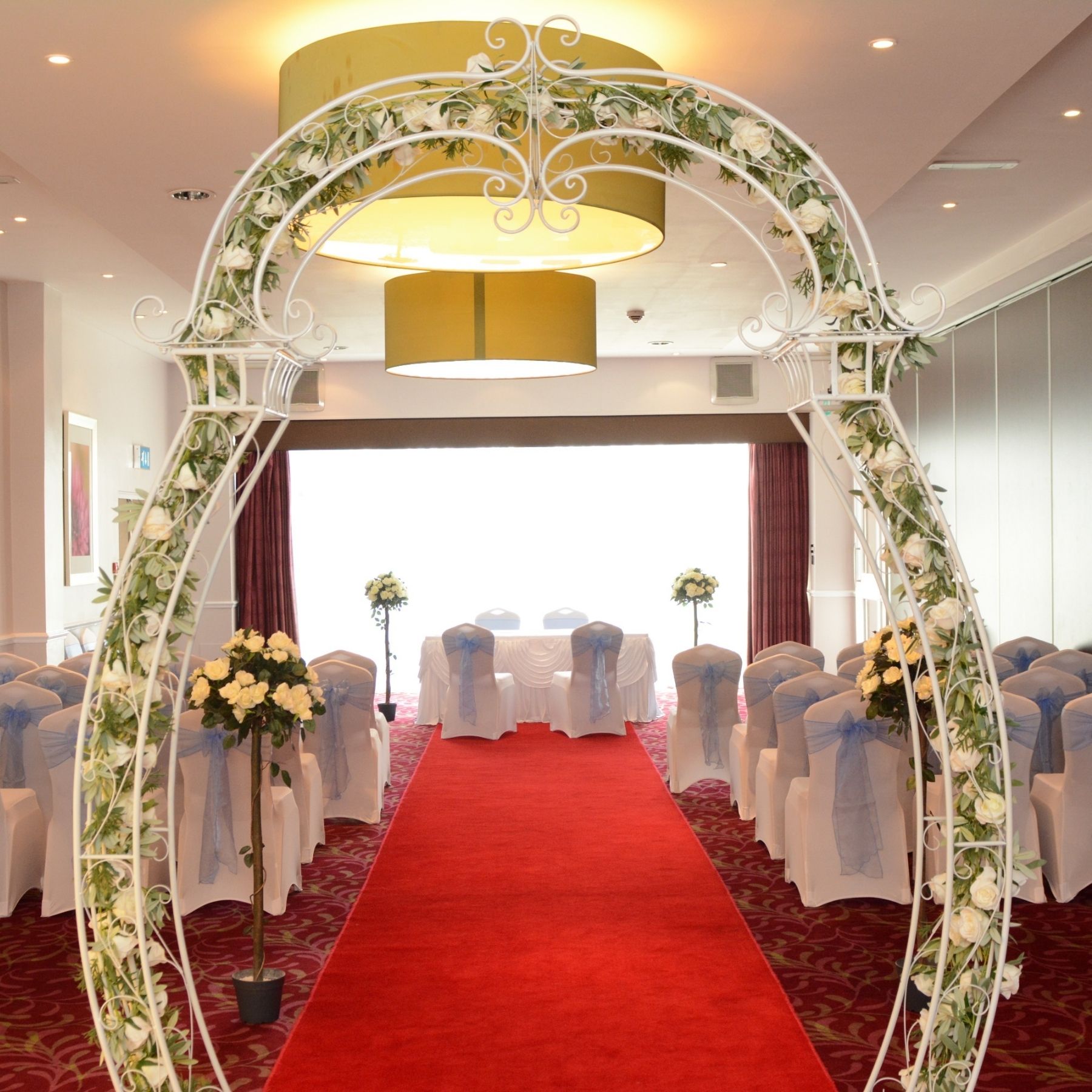 A wedding ceremony setup featuring a floral arch and a red carpet aisle.