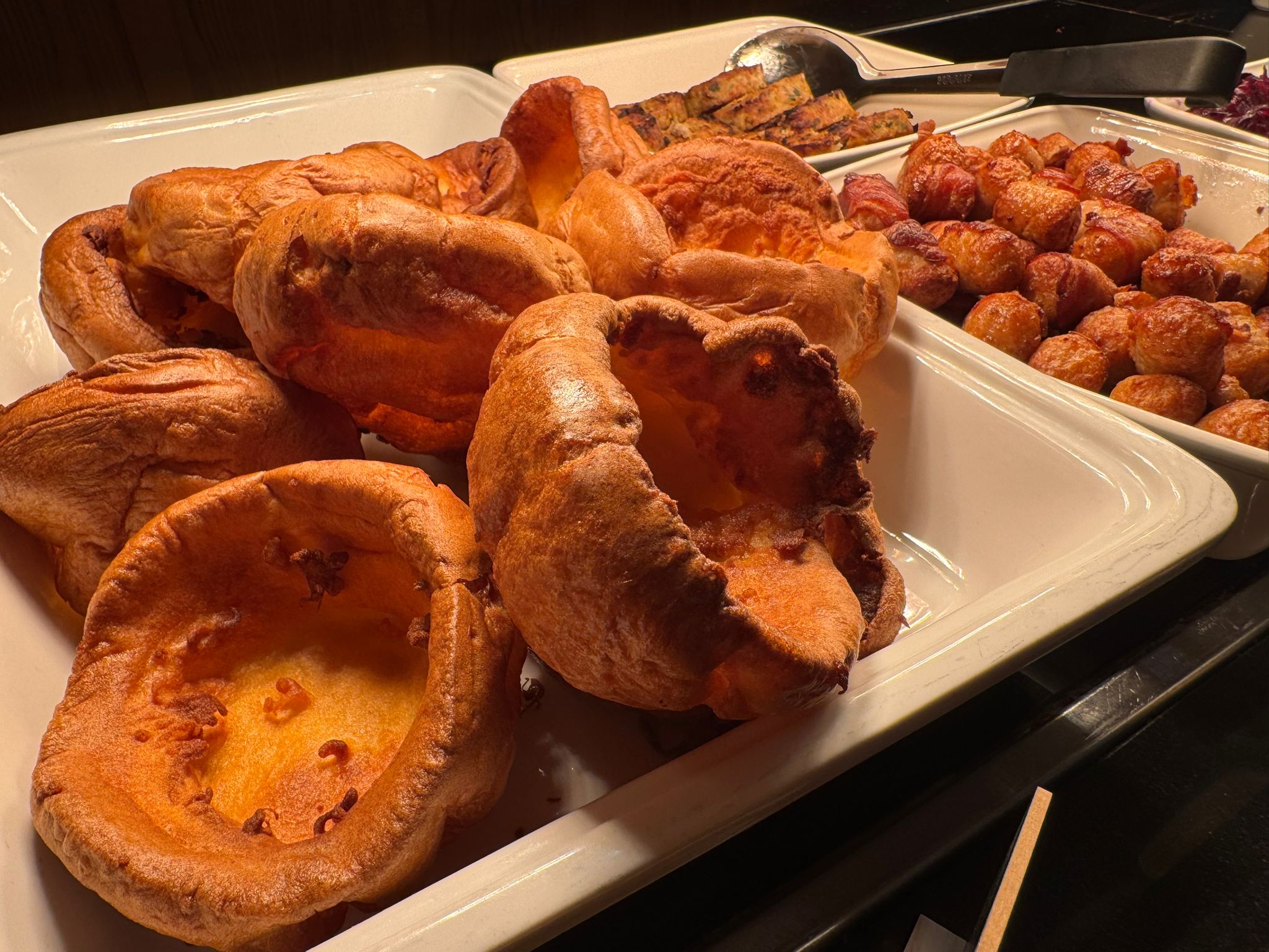 A close-up of several large, well-risen Yorkshire puddings in a white tray, showing their deep golden color and hollow centers.