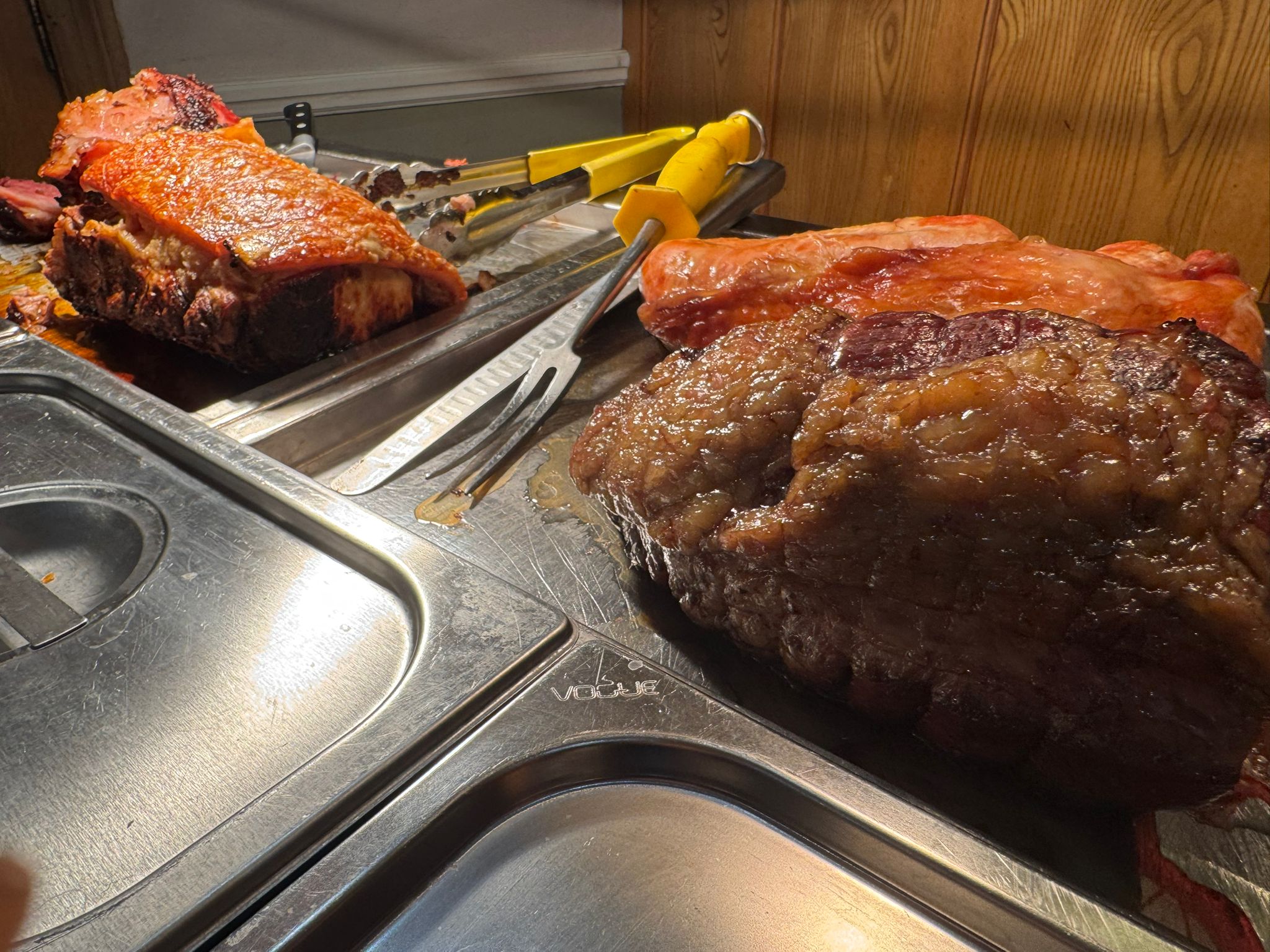A high-angle shot of various roasted meats and side dishes under warm heat lamps on a stainless steel buffet counter.