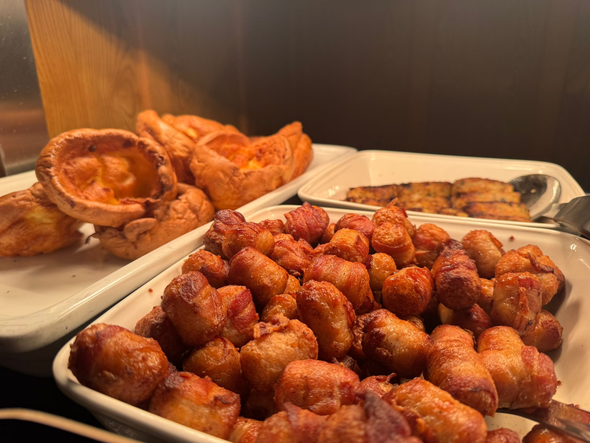 A close-up of golden-brown roasted potatoes and a large, crispy Yorkshire pudding in white serving dishes.